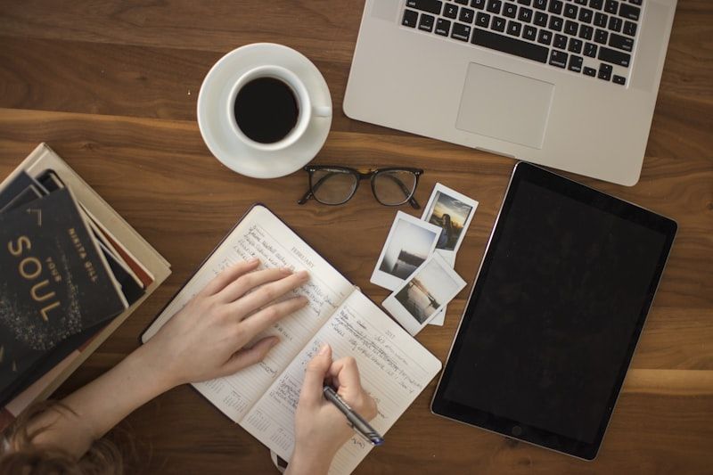 Overhead view of a desk with coffee, an open journal, and a laptop